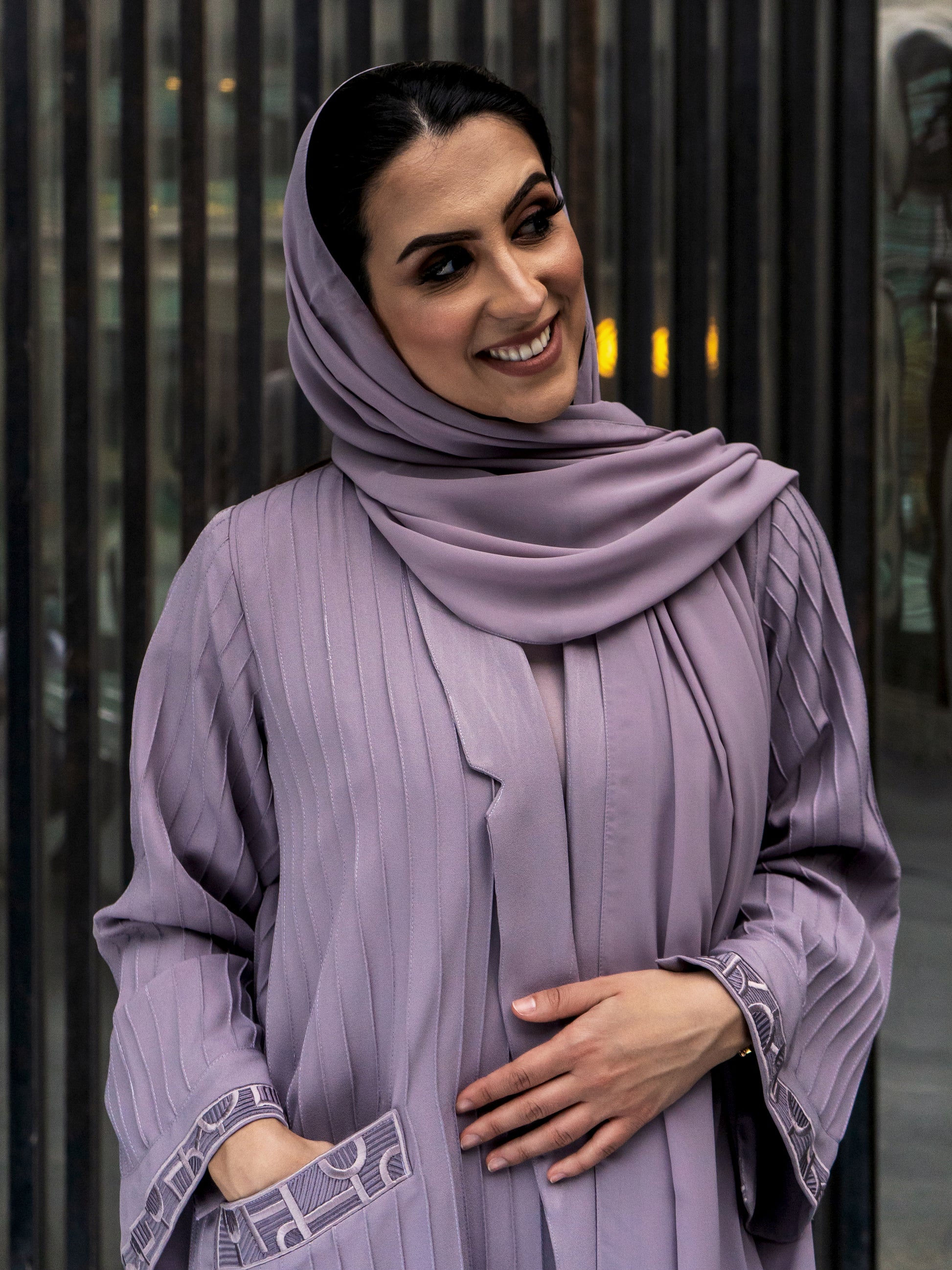 A woman wearing a gray abaya with embroidery details on the sleeves and matching headscarf.